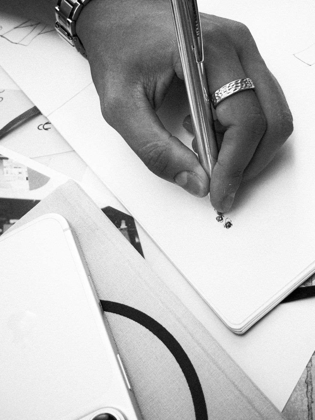 Une main portant une bague, en train de dessiner deux points dans un carnet.